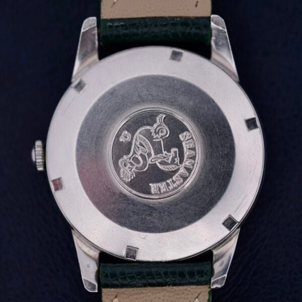 The image displays the back of a stainless steel Omega Seamaster 30 Caliber 286 watch case with an emblem of a seahorse and Seamaster engraving, paired with a black leather strap and beige underside.