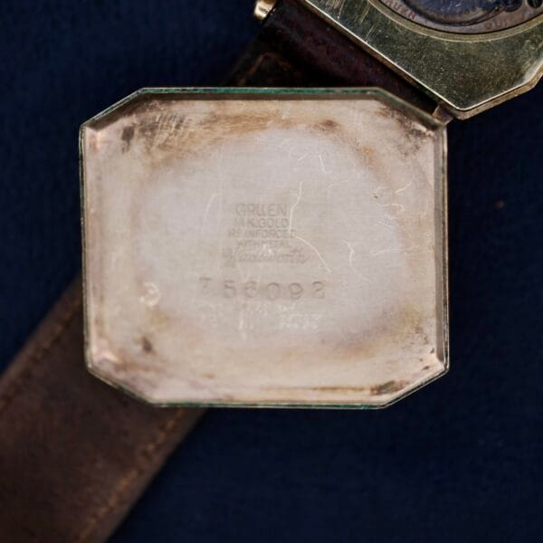 Close-up of the inside back cover of a Gruen Guild Art Deco Tank 14k watch case with engraved text: Gruen Guild 14K GOLD RE-INFORCED WRISTAL and the numbers 758092, featuring a worn leather strap.