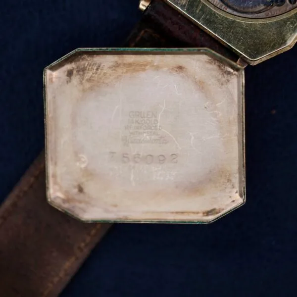 Close-up of the inside back cover of a Gruen Guild Art Deco Tank 14k watch case with engraved text: Gruen Guild 14K GOLD RE-INFORCED WRISTAL and the numbers 758092, featuring a worn leather strap.