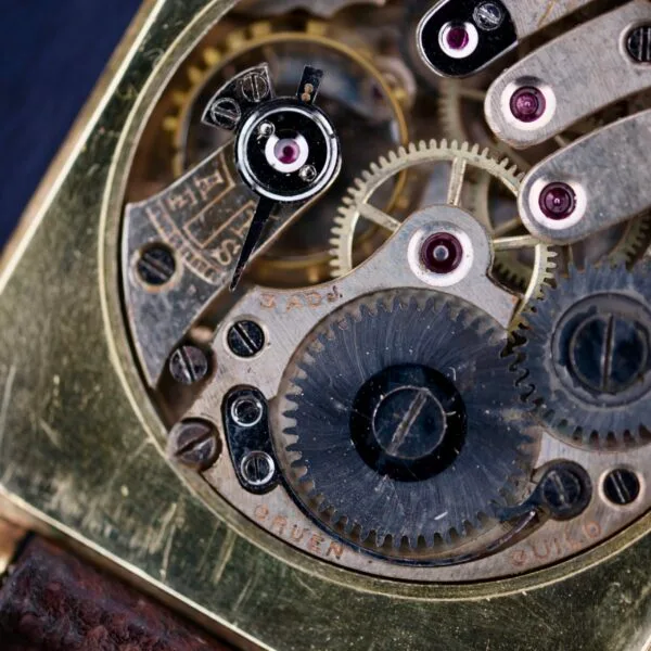 Close-up of the Gruen Guild Art Deco Tank 14k watch mechanism, featuring intricately arranged gears and cogs within a metallic frame, showcasing the timepieces craftsmanship and detailed textures.