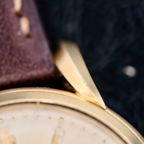 A close-up of the IWC Caltrava C. 89 18k Jumbo Case showcases its gold-toned elegance with a brown leather strap. The polished lug captures attention, enhancing its vintage charm, while the blurred background emphasizes the watchs rich textures and timeless appeal.