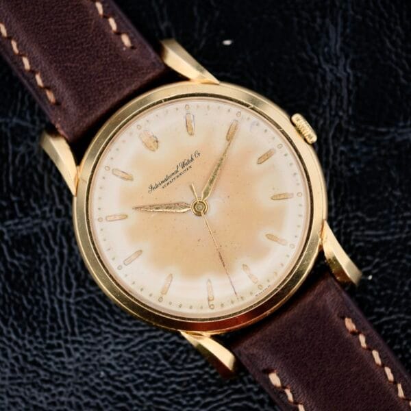 The Iwc Caltrava C. 89 18k Jumbo Case watch boasts a vintage gold aesthetic with a worn, off-white dial and gold hour markers. Its brown leather strap with white stitching enhances its timeless charm, while International Watch Co. on the face adds elegance and historical significance.