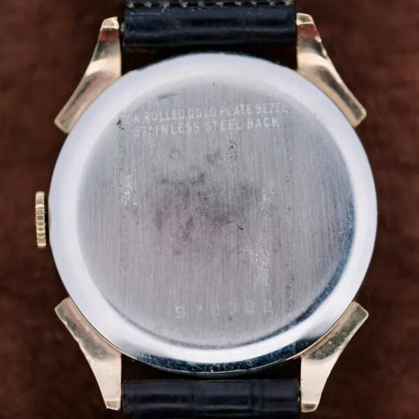The image features a vintage Benrus Day/Date Pointer wristwatch, displaying a silver case engraved with 10K ROLLED GOLD PLATE BEZEL and STAINLESS STEEL BACK, complemented by a black leather strap and serial number 912322.