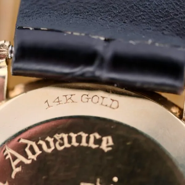 A close-up of the Tiffany & Co Arabic Numerals Dial T-101 watchs back shows 14K GOLD engraved on its gold surface, exuding elegance. A glimpse of the black leather strap enhances its timeless charm.