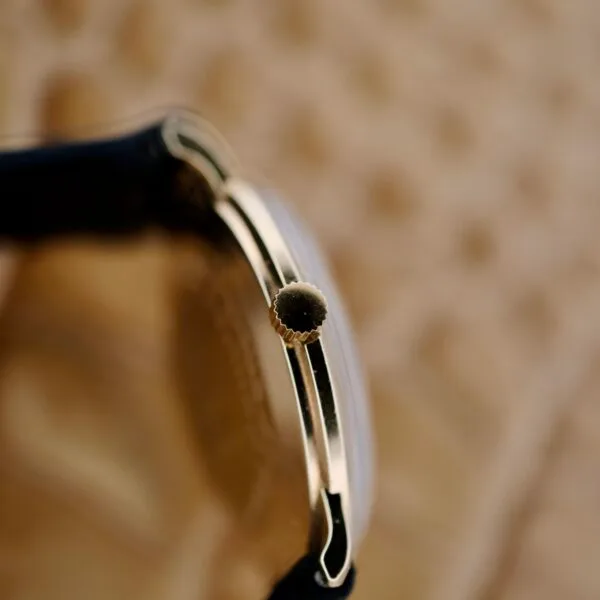 Close-up of the Tiffany & Co Arabic Numerals Dial T-101 shows a gold-colored case, textured crown, and possibly black strap. The blurred neutral background enhances the watchs elegant details.