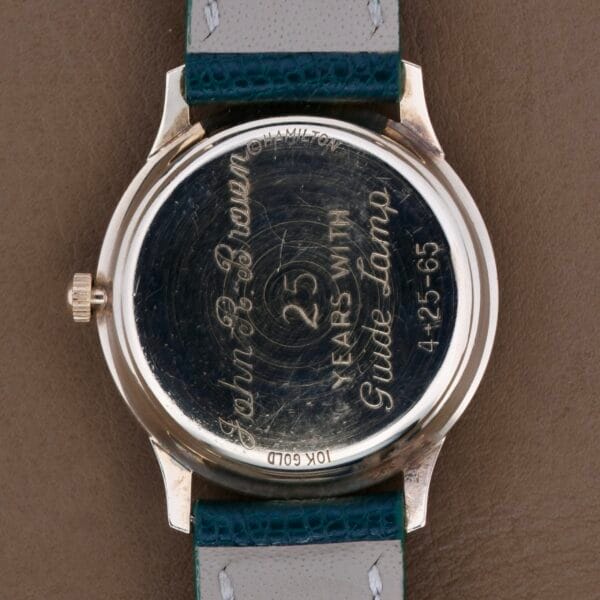 The Hamilton Masterpiece Thin-O-Matic 10k watchs back is engraved with John B. Brown, 25 years with Guido Lumber, and 4-25-65. It has a green and grey leather strap, showcasing elegance and history.