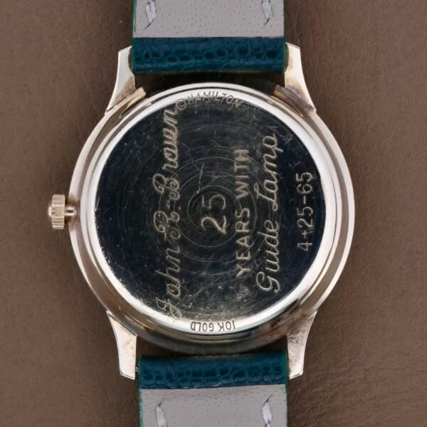 The Hamilton Masterpiece Thin-O-Matic 10k watchs back is engraved with John B. Brown, 25 years with Guido Lumber, and 4-25-65. It has a green and grey leather strap, showcasing elegance and history.