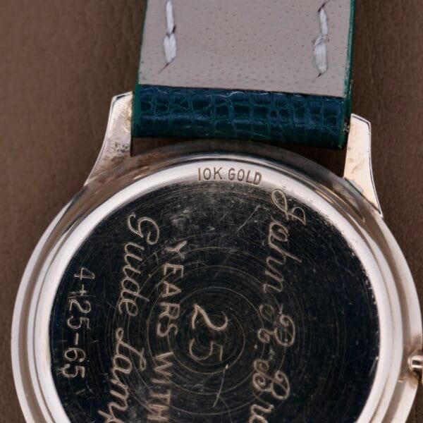 Close-up of a Hamilton Masterpiece Thin-O-Matic 10k watch back, engraved with 25 years with Guide Lamp 4-25-65 and John C. Brown, featuring a leather strap with visible stitching.