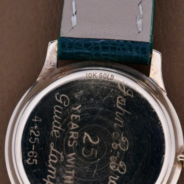 Close-up of a Hamilton Masterpiece Thin-O-Matic 10k watch back, engraved with 25 years with Guide Lamp 4-25-65 and John C. Brown, featuring a leather strap with visible stitching.