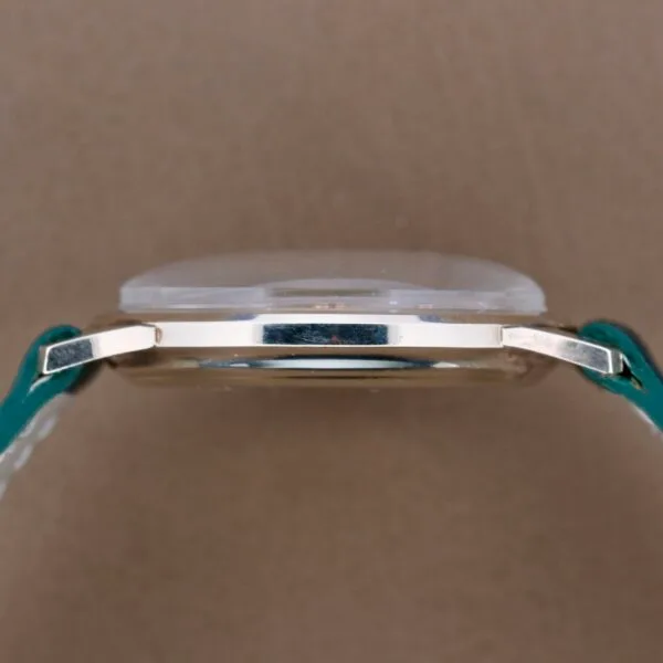 Side view of a Hamilton Masterpiece Thin-O-Matic 10k watch with a metal case and blue leather strap against a plain taupe background, embodying timeless elegance.