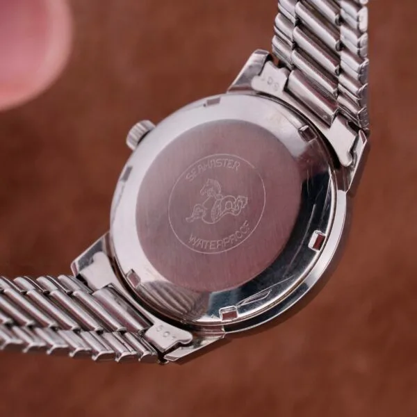 A close-up of the Omega Seamaster Automatic Date watch highlights its silver metal strap and an engraved seahorse design. The SEAMASTER WATERPROOF inscription accentuates its elegance, while the automatic date function adds precision and style.