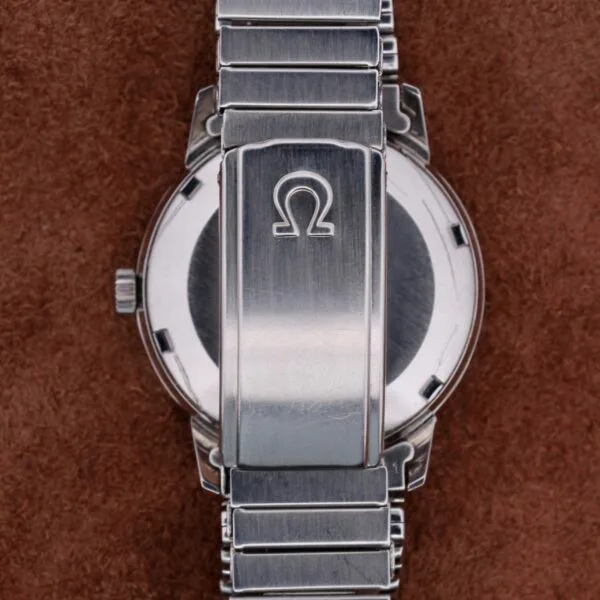 A close-up of the Omega Seamaster Automatic Dates silver band and case back, highlighting the iconic Omega logo on the clasp against a textured brown background, accentuating its metallic finish and automatic precision.