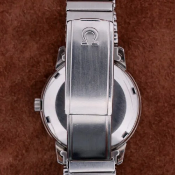 Close-up of a stainless steel clasp engraved with the Omega Seamaster Automatic Date logo, resting elegantly on a soft, brown fabric background.
