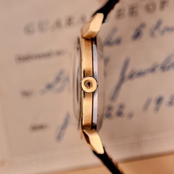 Side view of an Omega Seamaster Automatic Ref. 14350-2 Bull Horn Lugs gold watch with a black leather strap, set against a blurred document background.