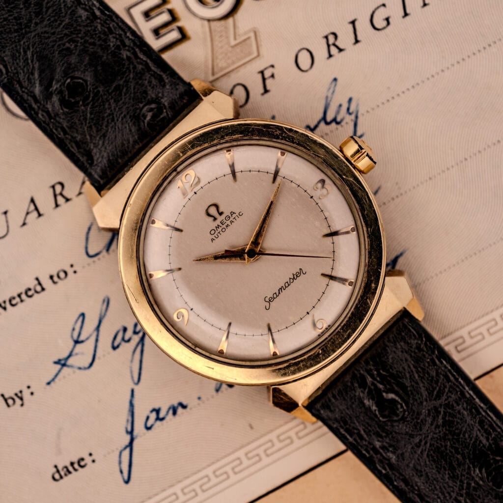 Omega Seamaster Automatic Ref. 14350-2 Bull Horn Lugs gold watch with black leather strap, elegantly displayed on its certificate of origin document.