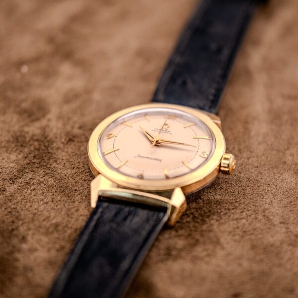 An Omega Seamaster Automatic Ref. 14350-2 Bull Horn Lugs wristwatch with a black leather strap rests elegantly on a brown suede surface.