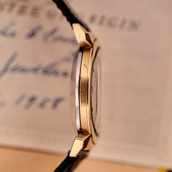 Side view of an Omega Seamaster Automatic Ref. 14350-2 Bull Horn Lugs gold case with black strap, displayed in front of a blurred document.