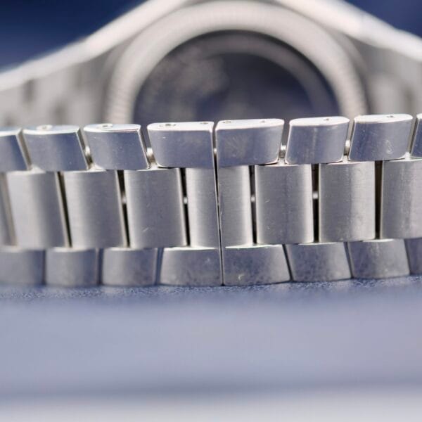 Close-up of the Baume Mercier Riviera 65580s silver metal bracelet with interlocking links, showcasing detailed texture and design, while the watch face is softly blurred in the background.