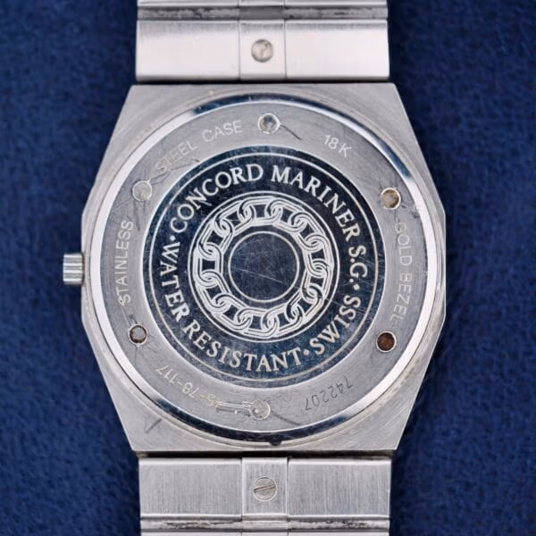 The image depicts the back of a Concord Mariner SG 18k Gold Bezel watch, showcasing engravings for Water Resistant Swiss, Stainless Steel Case, and an 18K Gold Bezel along with serial numbers; it features a central circular design.