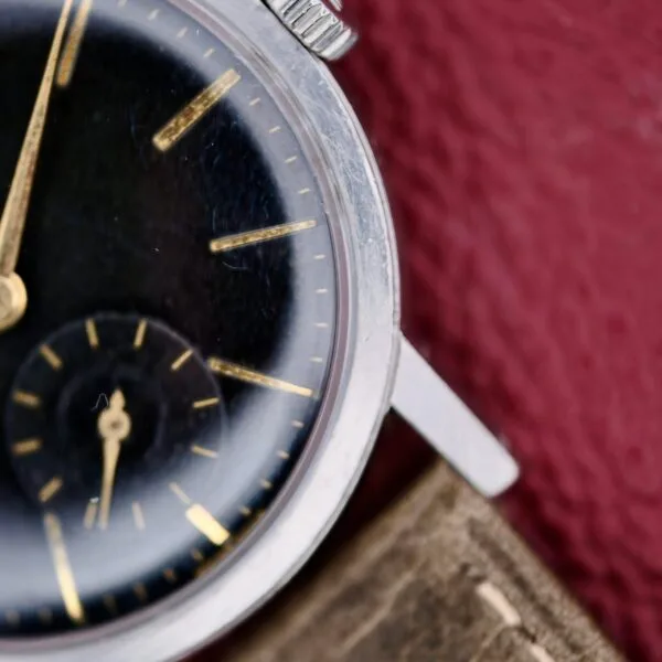 Close-up of the Tissot Seastar Black Gilt Dial Sub Second watch, featuring a black face with gold markers and hands, a silver casing, and a brown strap. The sub-dial displays the second hand against a textured red background.