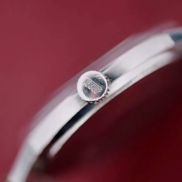 A close-up shows the silver watch crown engraved with Tissot from the Tissot Seastar Black Gilt Dial Sub Second. The background is muted red, while the focus highlights the crowns metallic texture.