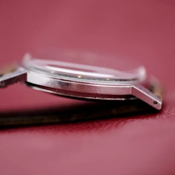 Close-up side view of the Tissot Seastar Black Gilt Dial Sub Second watch on a maroon leather surface, featuring a round face and metal case with short lugs and slightly raised glass. A leather strap is partially visible beneath the case.