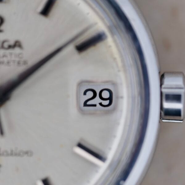 Close-up of the Omega Constellation Chronometer 14939-1 Flat Dial wristwatch face showing the date as 29, with a silver metallic case, black hour markers, partially visible brand name, and text indicating an automatic chronometer. The crown is positioned on the right side.