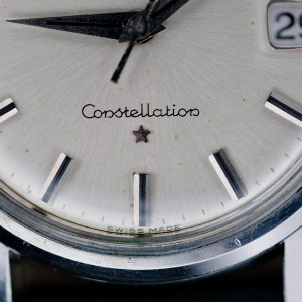 Close-up of an Omega Constellation Chronometer 14939-1 Flat Dial watch face, elegantly displaying the brand name with a small star beneath. The silver dial has black hour markers, a date window showing 28, and SWISS MADE etched at the bottom, epitomizing timeless craftsmanship.