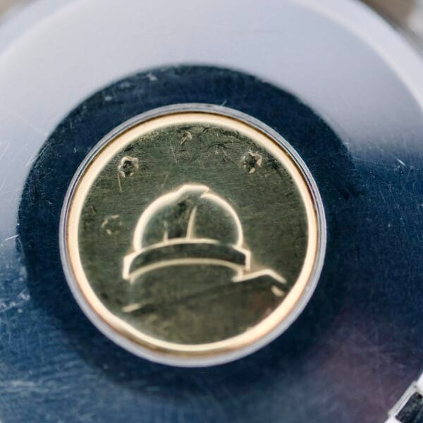 Close-up of a round, metallic button engraved with an astronaut helmet and stars, showcasing the celestial elegance of the Omega Constellation Chronometer 14939-1 Flat Dial, set against a dark, reflective surface.