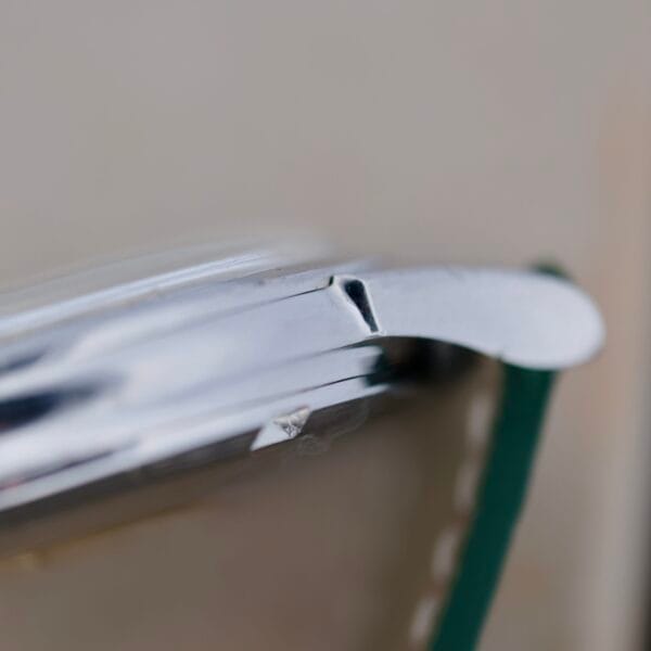 Close-up of an Omega Constellation Chronometer 14939-1 Flat Dial wristwatch, featuring a scratched bezel and a partially detached lug. The polished finish gleams subtly, with the green strap softly visible. The elegantly blurred background enhances its charm.