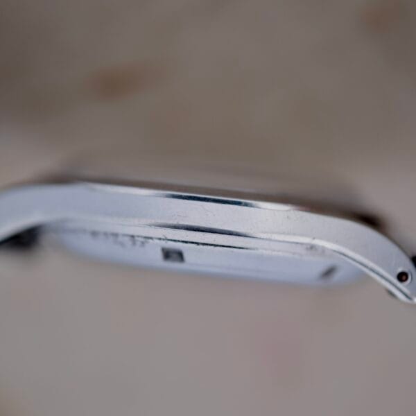 Close-up side view of a vintage Girard Perregaux Gyromatic 6169 Caliber 47 wristwatch. The metallic case shows some scratches and wear, with the watch face hidden, highlighting the edge and structure of this timeless timepiece.