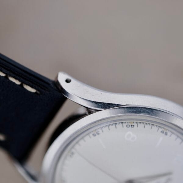 Close-up of a Girard Perregaux Gyromatic 6169 Caliber 47 vintage watch displaying a silver metallic frame and a black leather strap with white stitching. Its partially visible face features a classic white dial with thin silver hands, exuding timeless elegance.