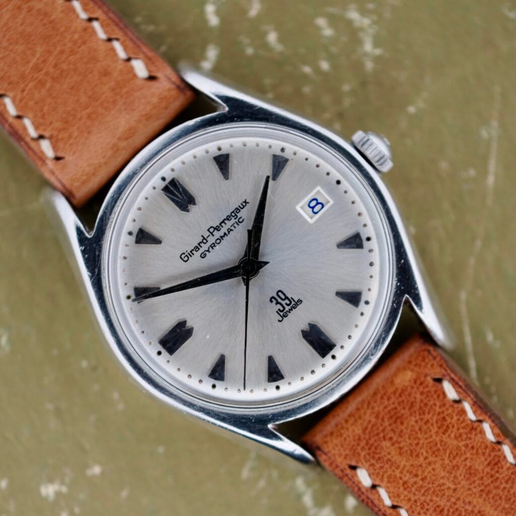 The Girard-Perregaux Gyromatic 39 Jewels wristwatch features a silver case, brown leather strap, date display, and 39 jewels.