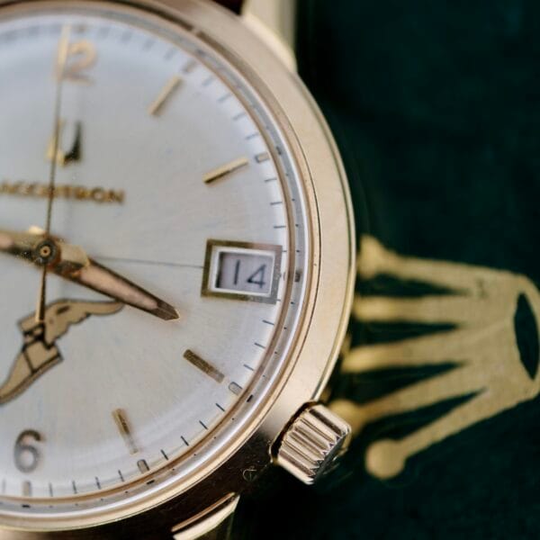 Close-up of a vintage luxury Bulova Accutron 218 Goodyear wristwatch featuring a white face and gold casing. The time is elegantly displayed with gold hour and minute hands, while a date window shows 14. The word Vacheron is partially visible on the classic dial.