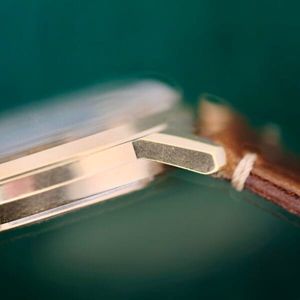 Close-up of the Bulova Accutron 218 Goodyear Dials vintage gold watch bezel with a brown leather strap attached by a spring bar. A dark green background highlights the elegance where the classic case meets the strap.