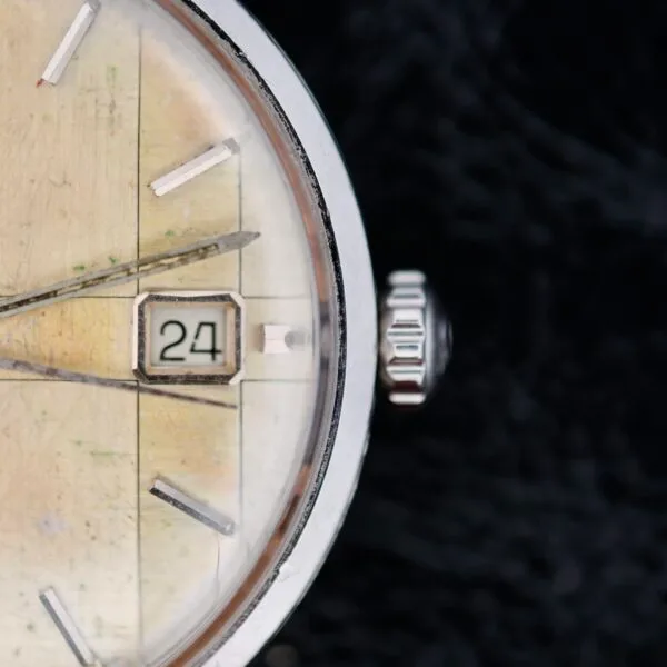 A close-up of an Omega Seamaster Deville Automatic 166.020 showcases a vintage analog watch face with a worn, off-white background, the time set at approximately 10:10 and the date reading 24. The silver case and crown provide elegance against a dark, textured backdrop.