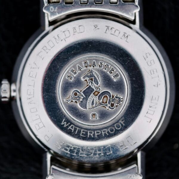 A close-up of the back of an Omega Seamaster Deville Automatic 166.020 displays an engraved horse and waves design with the text Seamaster and Waterproof, alongside P. Blomeley From Dad & Mum, June 1958.