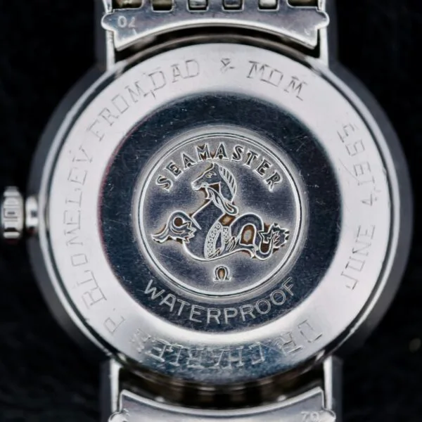 A close-up of the back of an Omega Seamaster Deville Automatic 166.020 displays an engraved horse and waves design with the text Seamaster and Waterproof, alongside P. Blomeley From Dad & Mum, June 1958.
