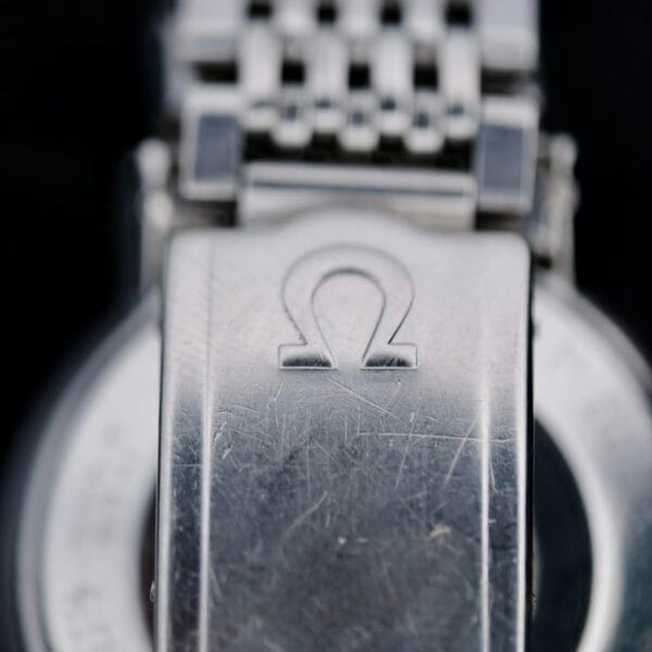 Close-up of a silver watch clasp with the engraved Omega symbol, attached to the metal link bracelet of an Omega Seamaster Deville Automatic 166.020. Scratches on the surface indicate wear.