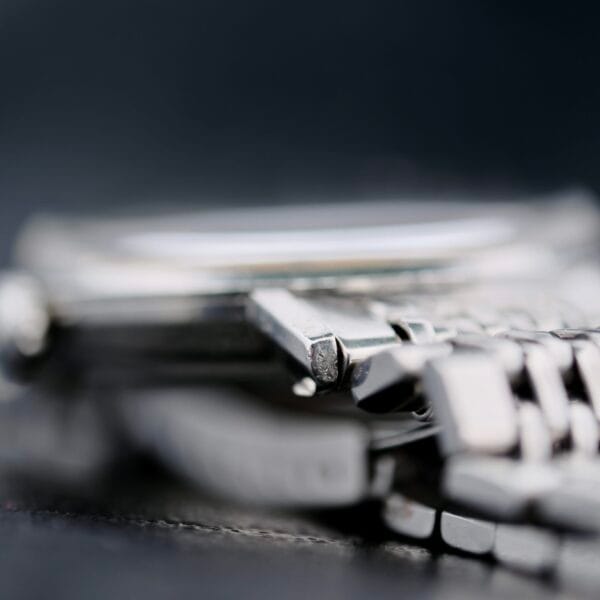 Close-up of the Omega Seamaster Deville Automatic 166.020 highlighting the silver metal case edge and part of the bracelet, with a slightly out-of-focus watch face against a blurred dark background.