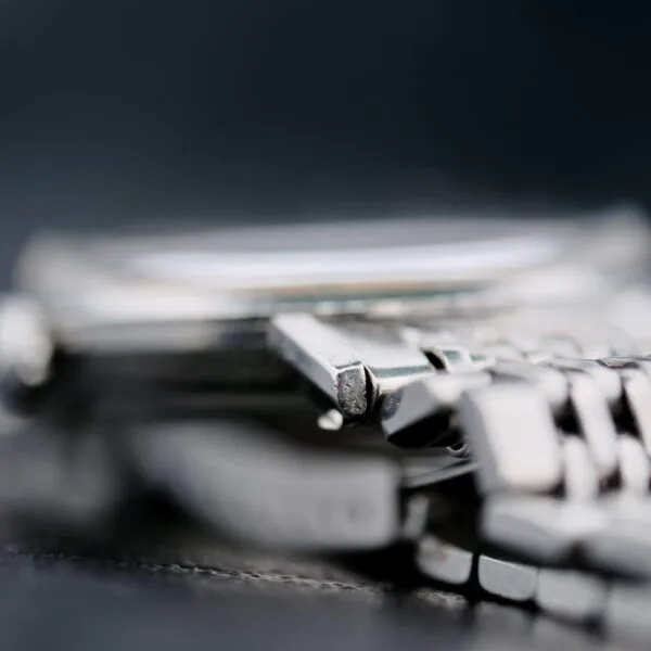 Close-up of the Omega Seamaster Deville Automatic 166.020 highlighting the silver metal case edge and part of the bracelet, with a slightly out-of-focus watch face against a blurred dark background.