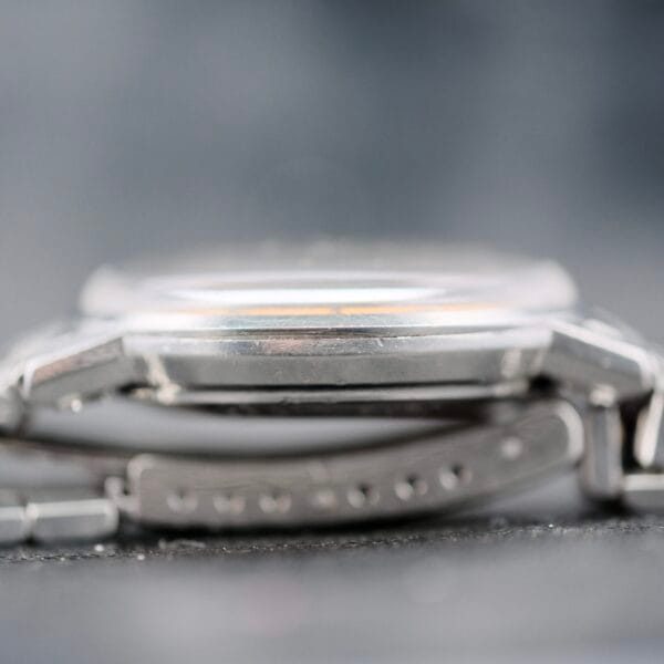 Close-up side view of an Omega Seamaster Deville Automatic 166.020 showing the watch case and metal bracelet, highlighting the edge of the case and adjustment holes on the bracelet against a blurred background.