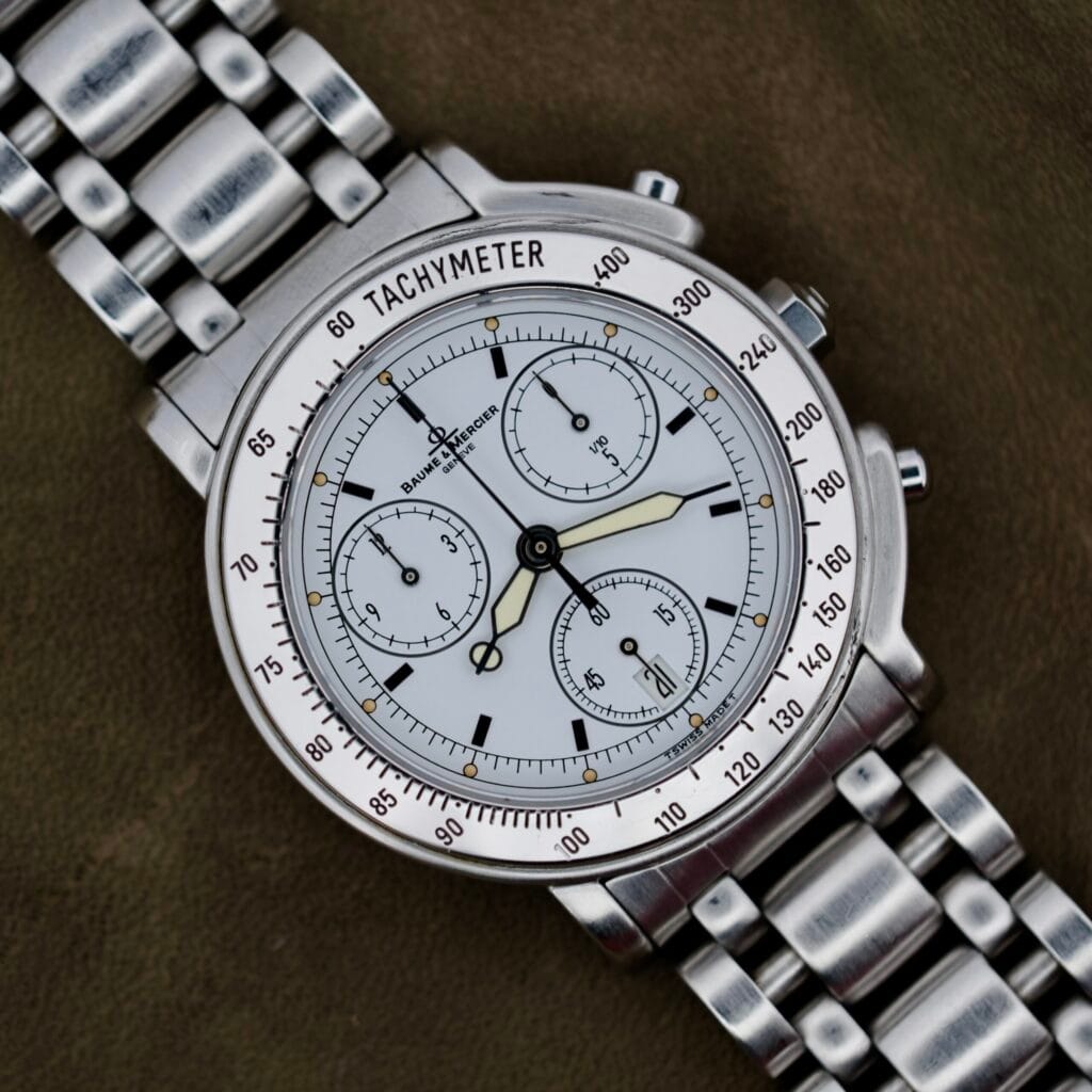 The Baume Mercier Formula S Chronograph features a silver-tone case, white dial, tachymeter bezel, and a sleek metal link bracelet.