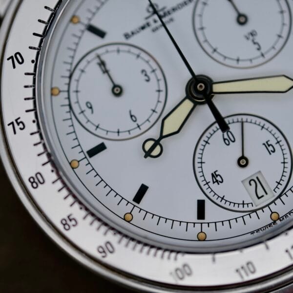 Close-up of the Baume Mercier Formula S Chronograph luxury watch, showcasing its white face with luminescent hands, a steel bezel with tachymeter markings, and a chronograph featuring three sub-dials plus a date window at 6 oclock.