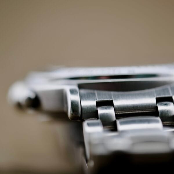 Close-up image of the Baume Mercier Formula S Chronographs stainless steel bracelet, showcasing its detailed brushed links. The link connections are prominently displayed against a blurred background to highlight the bracelet’s texture.