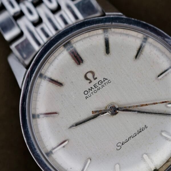 Close-up of an Omega Automatic Seamaster watch featuring a silver dial with simple hour markers and two hands. The Omega logo and Automatic sit at the top, while Seamaster is at the bottom, complemented by a silver metal strap.