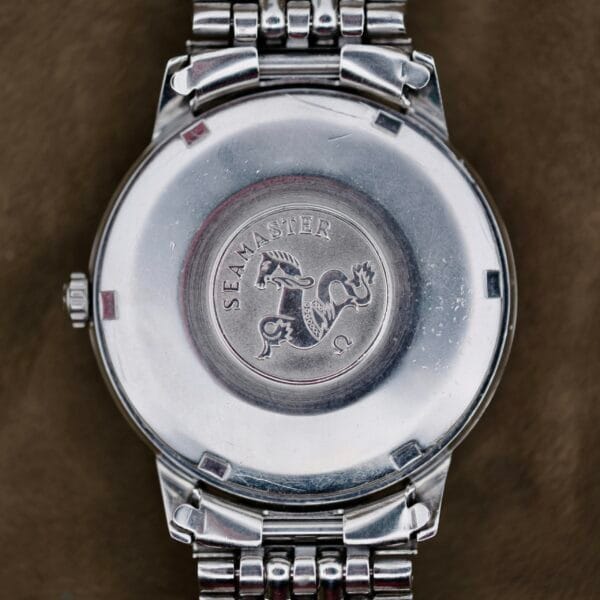 Close-up of the back of an Omega Automatic Seamaster wristwatch with a metal band, featuring an engraved logo that displays SEAMASTER and a stylized seahorse in a circular design.