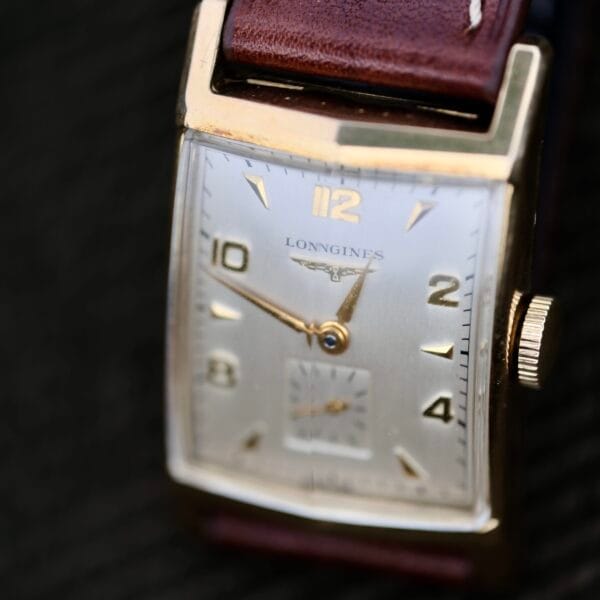 Close-up of a Longines Tank Manual Wind 22L wristwatch with a silver face, gold hour markers, small seconds subdial, brown leather strap, and gold trim. The time is approximately 1:50.