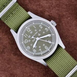 A Hamilton Khaki H3 Reference 9219 with a green nylon strap sits on a brown textured surface.