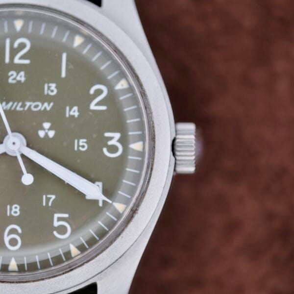 Close-up of a Hamilton Khaki H3 Reference 9219 wristwatch featuring a silver bezel, black dial with white Arabic numerals. The hour hand is near 5, and the minute hand is near 1. HAMILTON and a small radiation symbol are visible on the watch face.